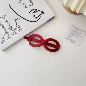 Close-up of matte vintage red infinity hair clip on white desk with aesthetic props