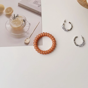 Brown spiral hair tie and silver C-shaped rhinestone earrings in a lifestyle setting