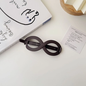 Detail view of the matte dark brown infinity shape hair clip on a minimalist white desk