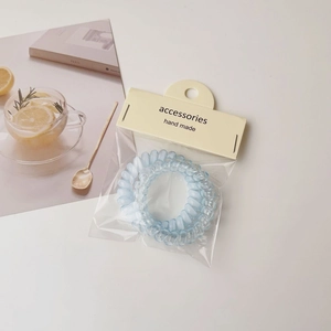 Close-up of two light blue spiral hair ties in transparent packaging on a stylish magazine