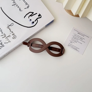 Detail view of a matte infinity loop hair clip in deep chocolate brown on a minimalist background