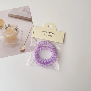 Detail of two purple spiral hair ties in handmade packaging on a lifestyle background