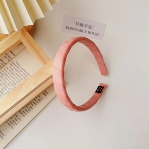Close-up of pink fabric pleated headband with brand tag and minimalist aesthetic