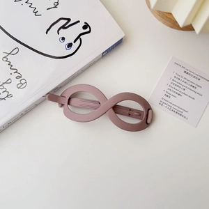 Detail view of pink matte infinity hair clip on white desk with aesthetic props
