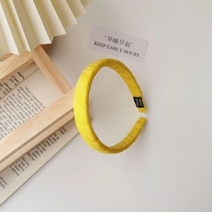 Close-up of yellow fabric headband with handmade label on a minimalist aesthetic background