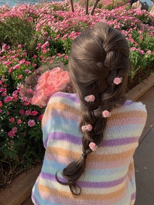 Detailed view of pink rose mini hair claws styled on a French braid in a garden