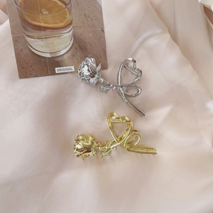 Close-up of elegant gold and silver metal rose claw clips on pink silk fabric background