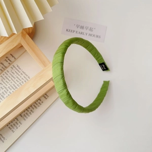 Close-up detail of green fabric headband showing pleated texture and woven inner label