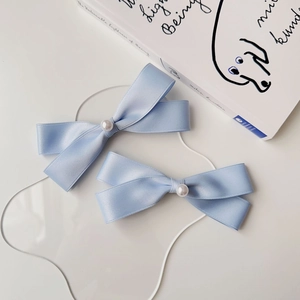 Set di due fermagli per capelli con fiocchi di raso azzurro e perle su sfondo bianco