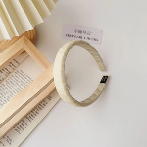 Close-up of beige pleated fabric headband with textured vertical stripes and black label
