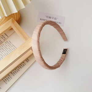 Detailed macro view of beige pleated fabric headband featuring a black handmade textile label