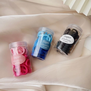 Three jars of colorful high-elasticity hair ties on a soft satin fabric background