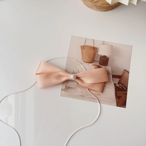 Dettaglio del fermaglio a fiocco in raso rosa champagne con perla bianca su sfondo elegante