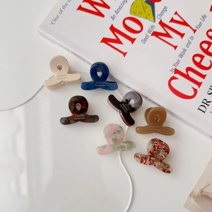 Mini acetate hair claws in various colors and patterns on a transparent tray