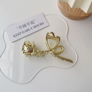 Close-up of golden metal rose flower hair claw clip with heart shaped handle detail