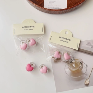 Close-up of pink heart-shaped hair clips in packaging on a white desk with props