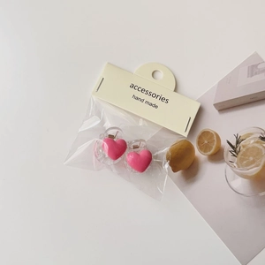 Close-up of two pink heart hair clips with handmade accessories packaging on beige background
