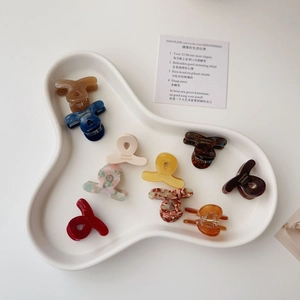 Mini acetate hair claw clips in various colors and tortoiseshell patterns on ceramic tray