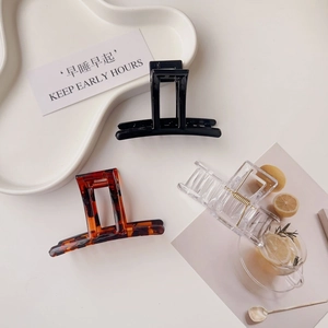 Detailed view of black, amber, and clear acrylic hair claws on a minimalist white tray