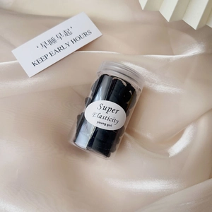 Jar of high-elastic black hair ties on beige silk with decorative lifestyle elements