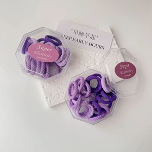 Detail view of purple elastic hair ties in a clear hexagonal box on a white background
