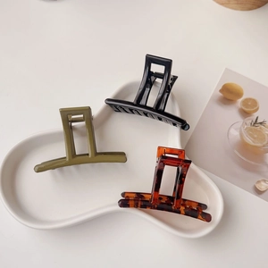 Close-up of three matte acrylic hair claws in olive green, black, and tortoise shell