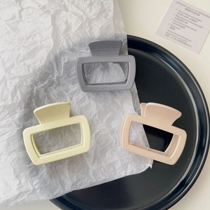 Three matte resin hair claws in grey, pale yellow and dusty pink on a black display tray