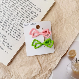 Détail des barrettes nœud en alliage mat rose et vert présentées sur une carte papier