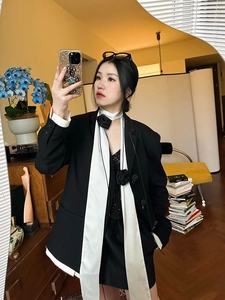Détail d'une veste noire avec revers en satin blanc et une broche de rose en tissu 3D
