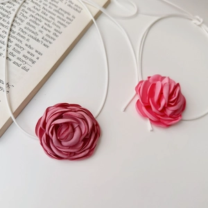 Détail d'un choker rose en tissu artisanal avec pétales délicats et ruban blanc
