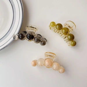 Close-up of three amber textured claw clips in grey, olive green and peach pink tones