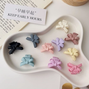 Set of ten colorful matte bow mini hair clips on a white ceramic tray for women