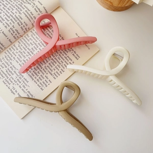 Three large matte shark hair clips in pink, beige, and khaki on an open book