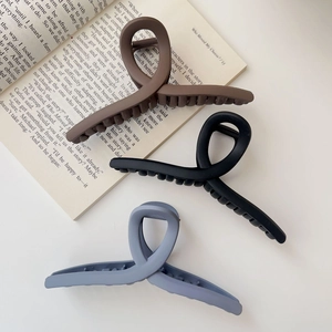 Three matte large shark hair clips in coffee brown, black and grey on a book background