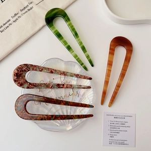 Detail of U-shaped acetate hairpins in amber and marble patterns with French logo