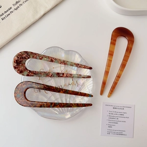 Detailed shot of three acetate U-shaped hair pins with tortoiseshell patterns on a shell tray