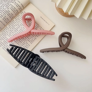 Three large matte hair claws in pink brown and black colors displayed on a book