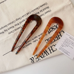 Detail of two U-shaped acetate hair pins in tortoiseshell and amber patterns