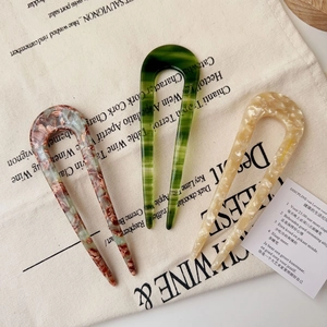 Detailed macro view of three acetate U-shaped hair pins on a beige fabric bag background
