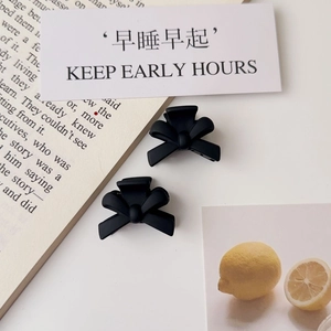 Close-up of dual matte black bow hair clips on a minimalist French lifestyle background