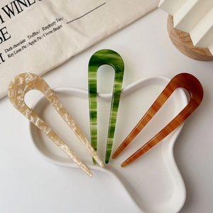 Three acetate U-shaped hair pins with marble patterns in a stylish ceramic tray