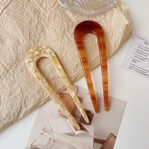 Detail of cream marble and amber tortoiseshell U-shaped acetate hair pins on neutral background