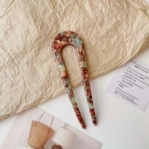 Close-up of acetate U-shaped hair fork with green marble texture and gold lettering