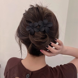 Gros plan de deux pinces à cheveux fleurs noires mates portées par une femme