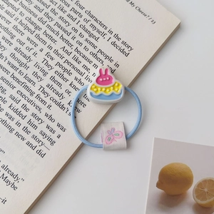 Détail d'un élastique à cheveux bleu avec breloque lapin rose et étiquette papillon