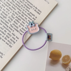 Gros plan d'un élastique à cheveux violet avec un ours et une étiquette en tissu bleu