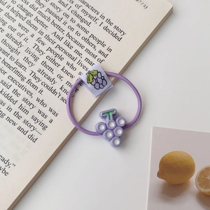 Détail de l'élastique à cheveux violet avec breloque raisin et étiquette en tissu brodée