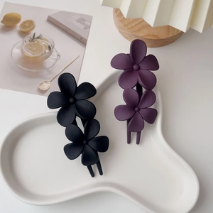 Détail de pinces à cheveux fleurs mates en noir et violet foncé sur une assiette en céramique