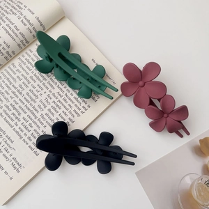 Gros plan de trois pinces à cheveux à fleurs mates en vert foncé, rouge et noir