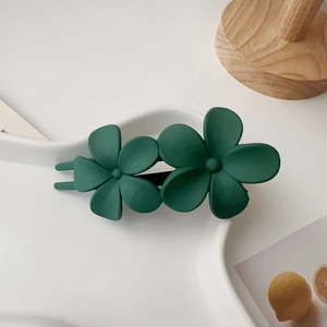 Détail de la barrette à cheveux double fleur vert foncé mat sur une assiette blanche